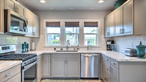 Cocina moderna con armarios blancos, electrodomésticos de acero inoxidable y una ventana con persianas.