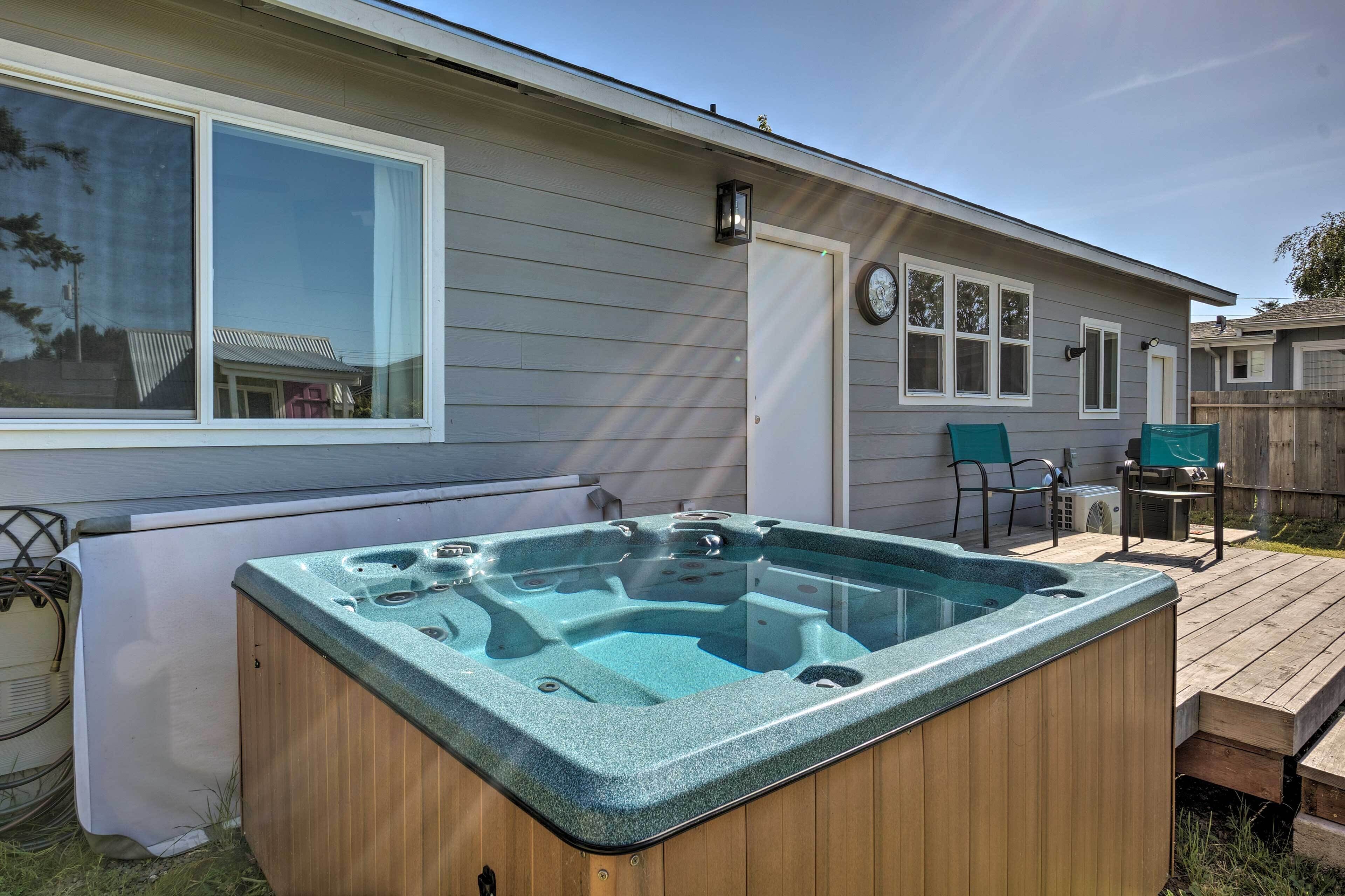 A wooden hot tub in a backyard with a deck, a window, and a door.