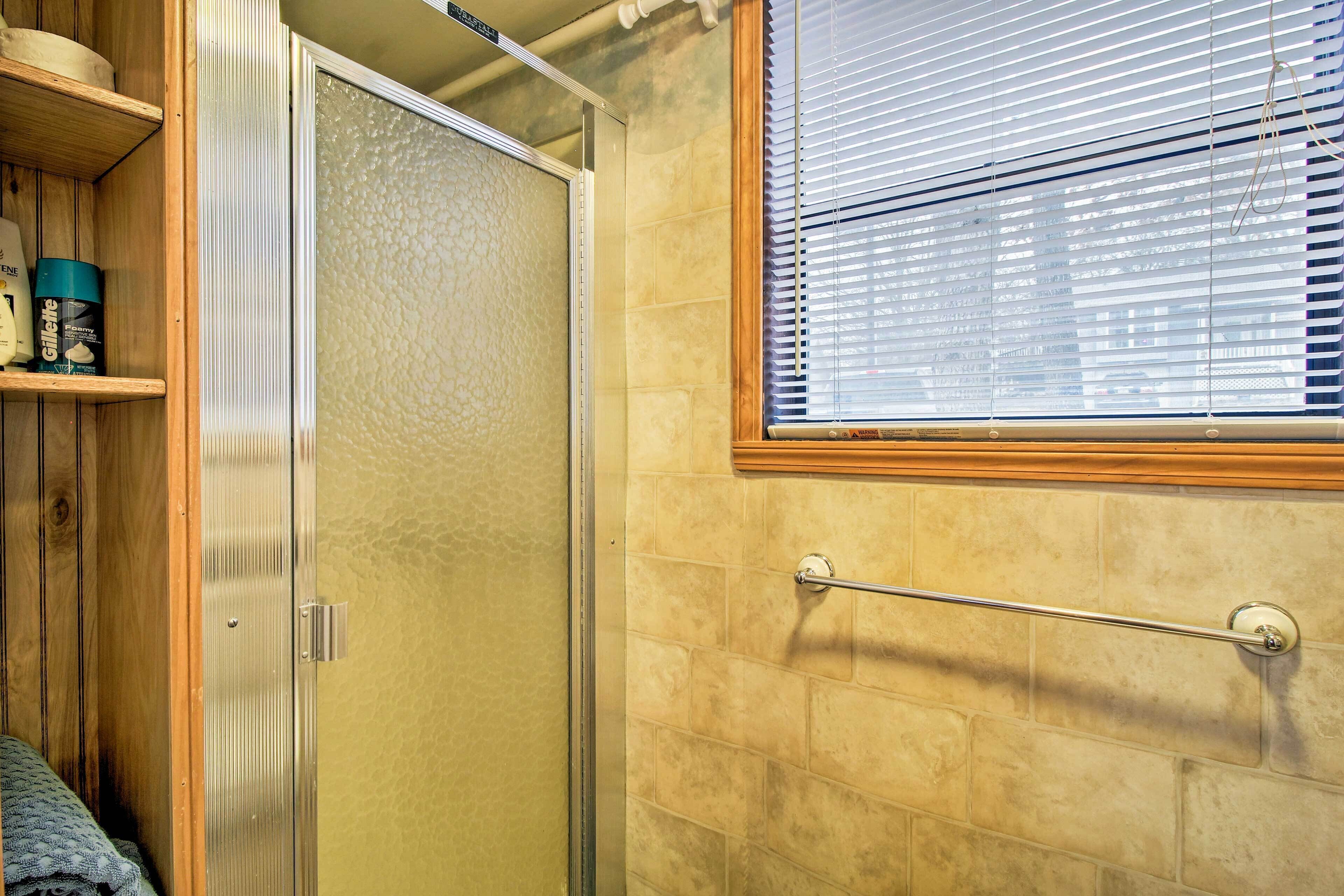 Une salle de bain avec une douche, des étagères en bois, un porte-serviettes et une fenêtre avec des stores.