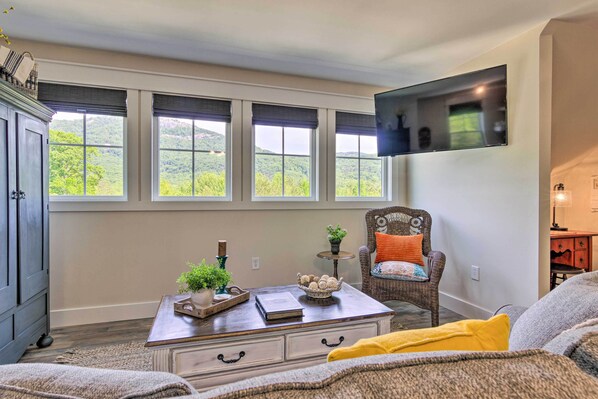 A living room with a large window, a flat-screen TV, a wooden coffee table, and a wicker chair. - Near Parks, Trails & Lakes: Quaint Landrum Escape! (Landrum)