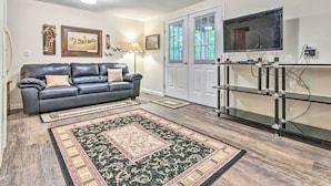 A living room with a leather sofa, two rugs, a TV on a stand, and a door with windows. - Deck w/ Bbq: Hot Springs Village Apt! (Hot Springs Village)