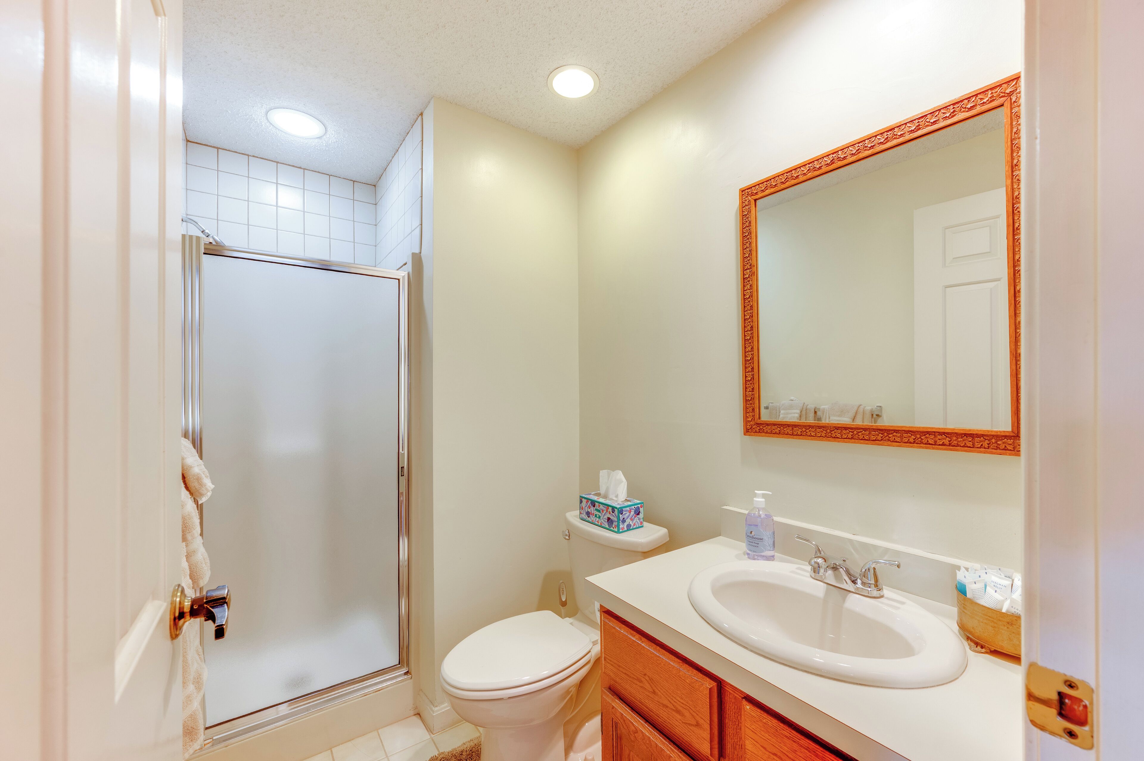 A bathroom with a shower, toilet, sink, and a mirror with a decorative frame.