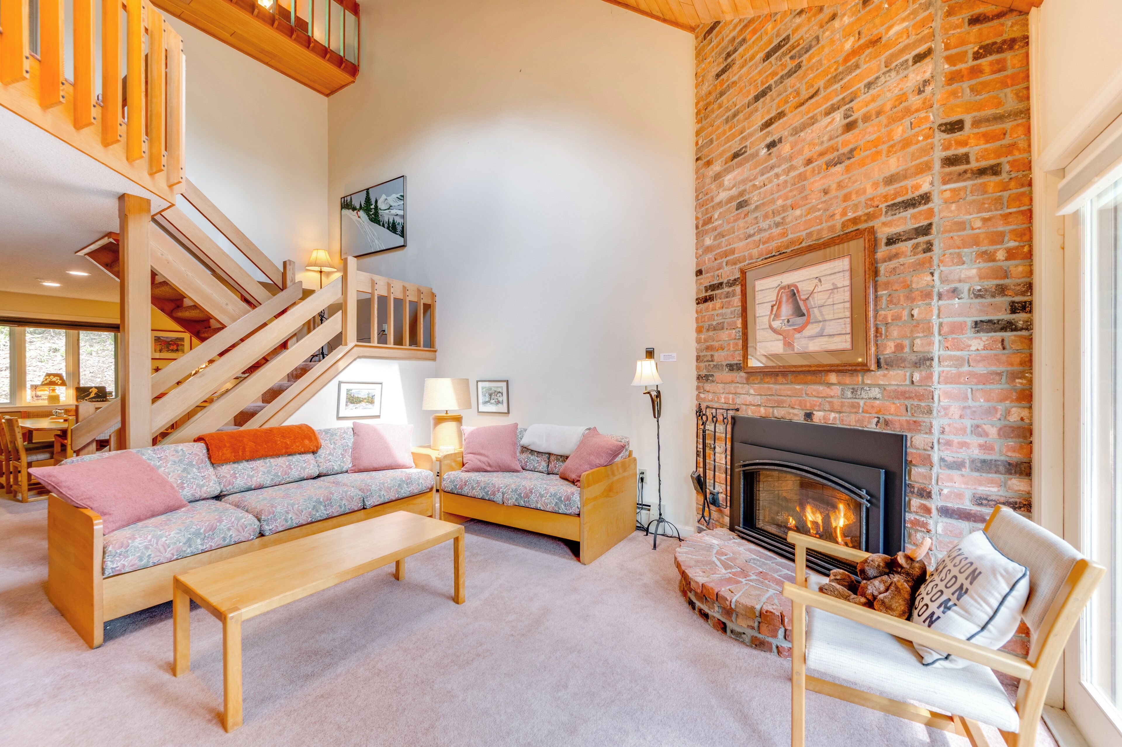 A cozy living room with a wooden staircase, a fireplace, and a sofa set.