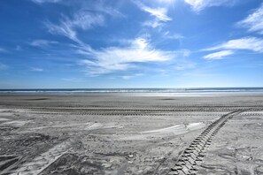 Une plage avec un ciel dégagé et des empreintes de pas bien visibles qui mènent à l’eau.