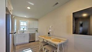 Une cuisine moderne avec des meubles blancs, un réfrigérateur en acier inoxydable et une table à manger en bois accompagnée de deux bancs.