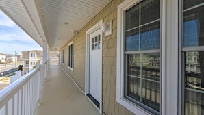 Une véranda couverte avec une balustrade blanche, un revêtement de couleur beige et de grandes fenêtres.