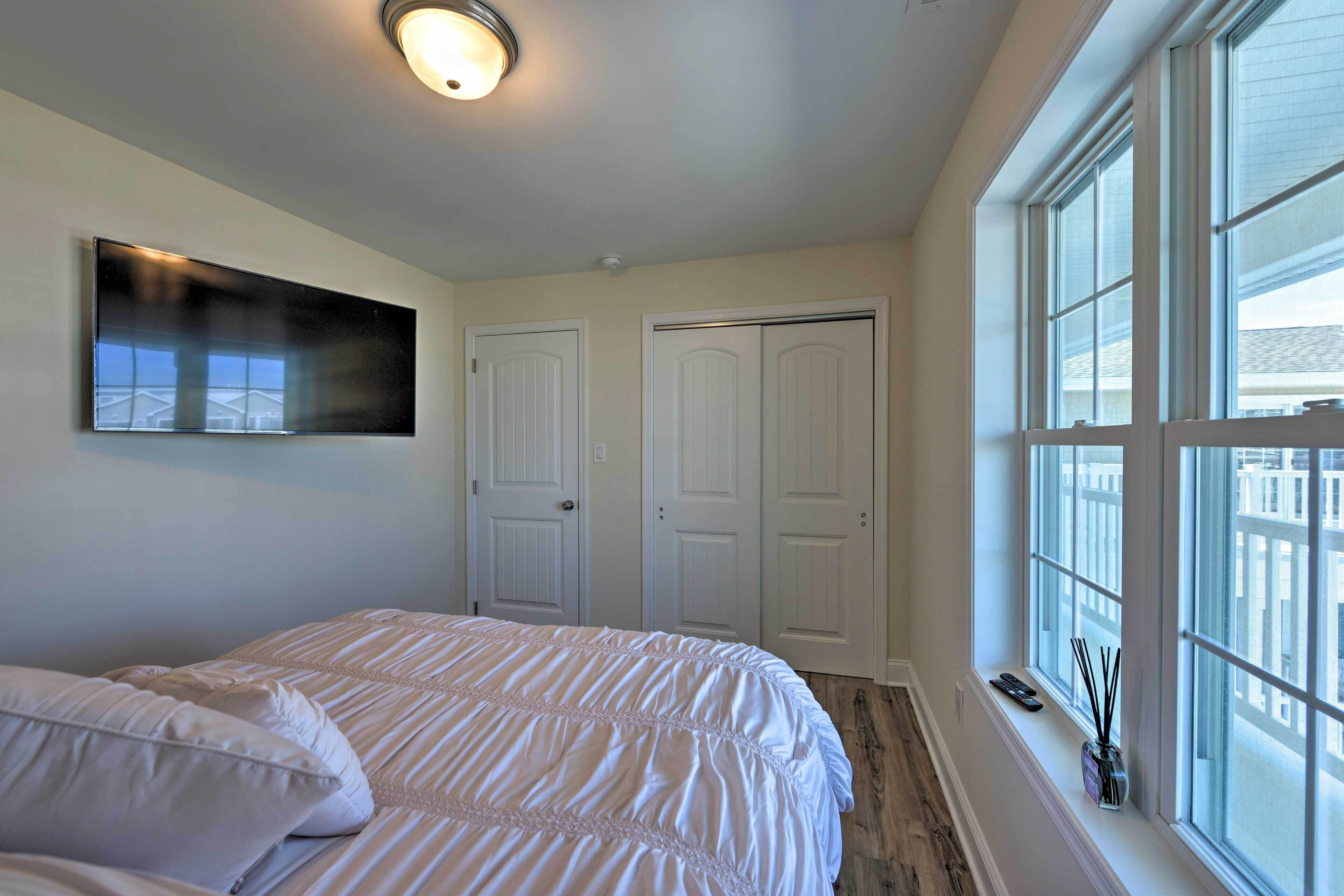 A bedroom with a bed, a TV mounted on the wall, and a window with a view of buildings.