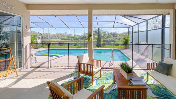 A sunlit patio with a pool, wooden furniture, and a view of the surrounding landscape. - Bright & Sunny Riverview Oasis w/ Pool & Pond (Riverview)