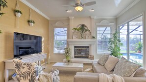 A living room with a flat-screen TV, a fireplace, a ceiling fan, and large windows. - Bright & Sunny Riverview Oasis w/ Pool & Pond (Riverview)