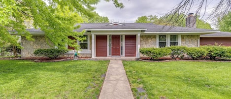 A single-story house with a stone facade, a red front door, and a front yard with a concrete pathway leading to the entrance.