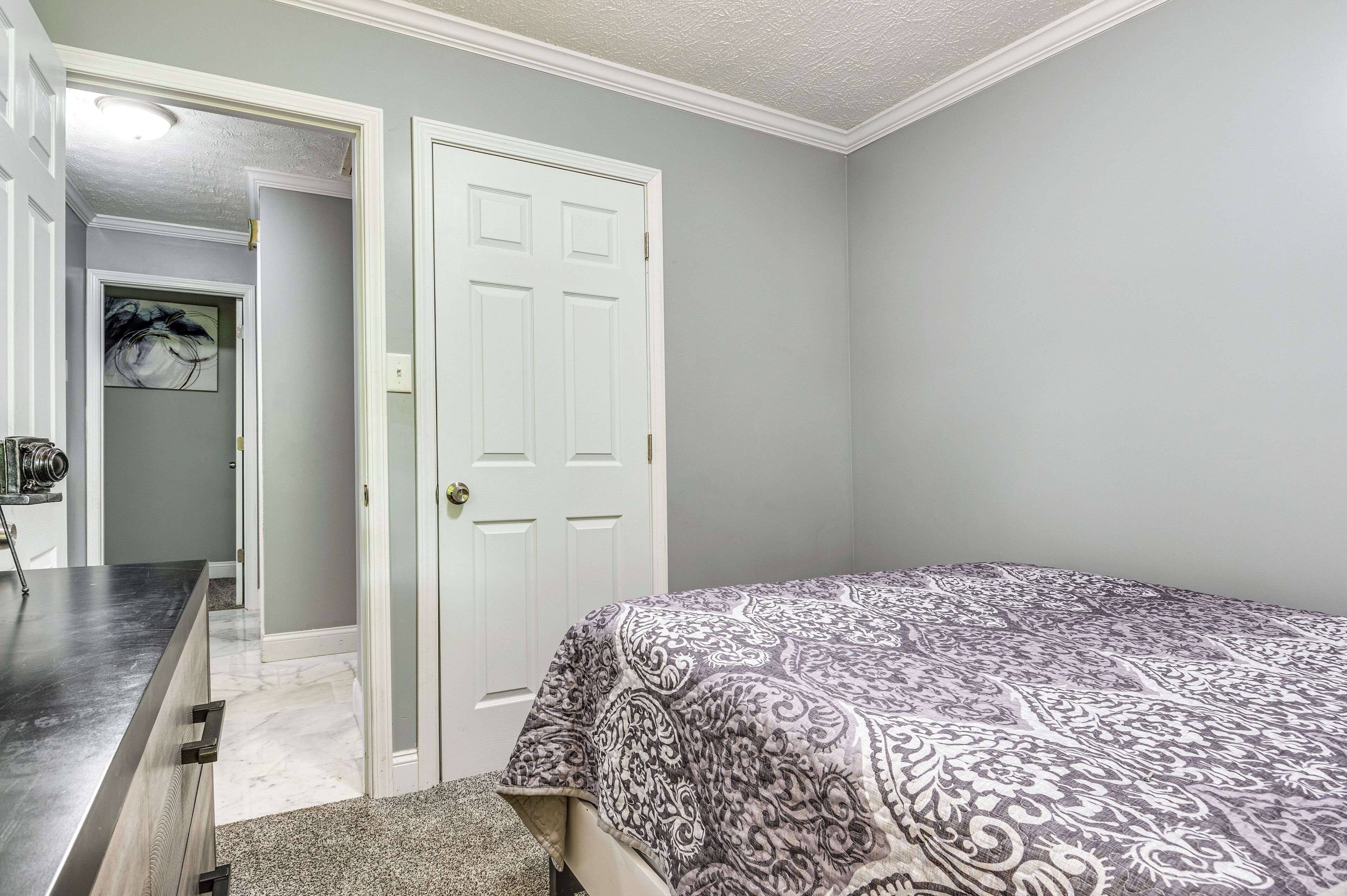 A bedroom with a bed, a dresser, and a door leading to another room.