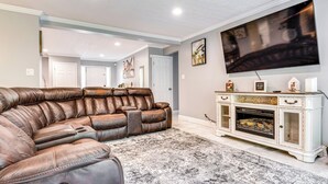 A living room with a brown leather sectional sofa, a large flat-screen TV mounted on the wall, and a white entertainment center with a fireplace. - Indianapolis Vacation Rental ~ 8 Mi to Downtown! (Indianapolis)