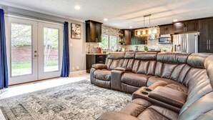A modern living room with a sectional sofa, a kitchen with dark cabinets, and a large window with curtains. - Indianapolis Vacation Rental ~ 8 Mi to Downtown! (Indianapolis)