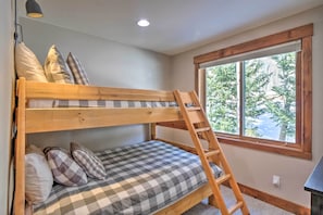A bunk bed with a wooden ladder, checkered bedding, and a window with a view of trees.