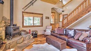 A cozy living room with a stone fireplace, leather sofa, and a wooden staircase. - Rustic Mountain Sanctuary on 2+ Acres w/ Deck! (Alma)