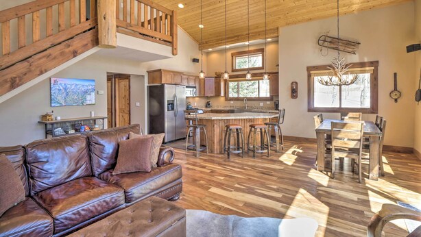 A spacious living area with a leather sofa, wooden staircase, kitchen, and dining area. - Rustic Mountain Sanctuary on 2+ Acres w/ Deck! (Alma)