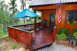 Uma cabana de madeira com um alpendre coberto, churrasqueira e uma bandeira americana.