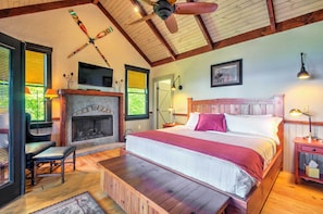 Quarto com cama grande, piso de madeira, lareira e ventilador de teto.