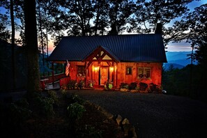 Uma cabana de madeira com telhado de metal, rodeada por árvores e um caminho de acesso de brita.