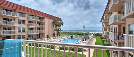 Zona de piscina con vista al océano, rodeada de edificios de varios pisos con balcones.