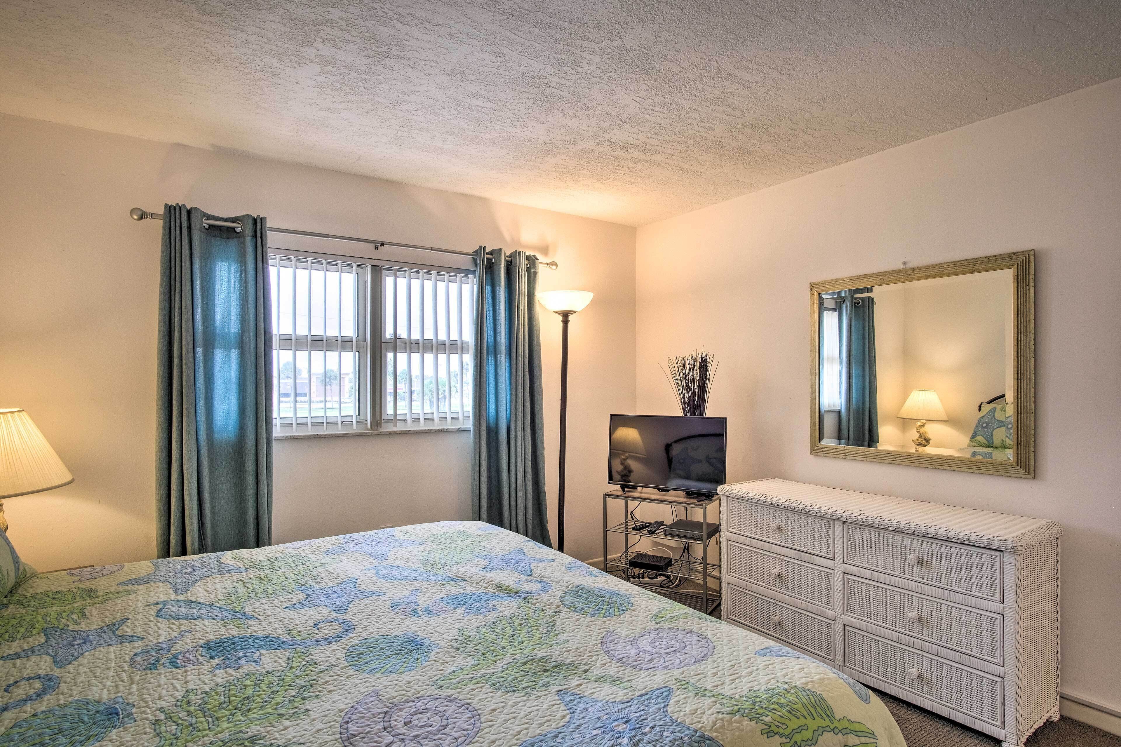A bedroom with a bed, a dresser, a television, and a mirror.