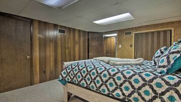 A bedroom with a wooden panel wall, a bed with patterned bedding, and a ceiling with fluorescent lighting.