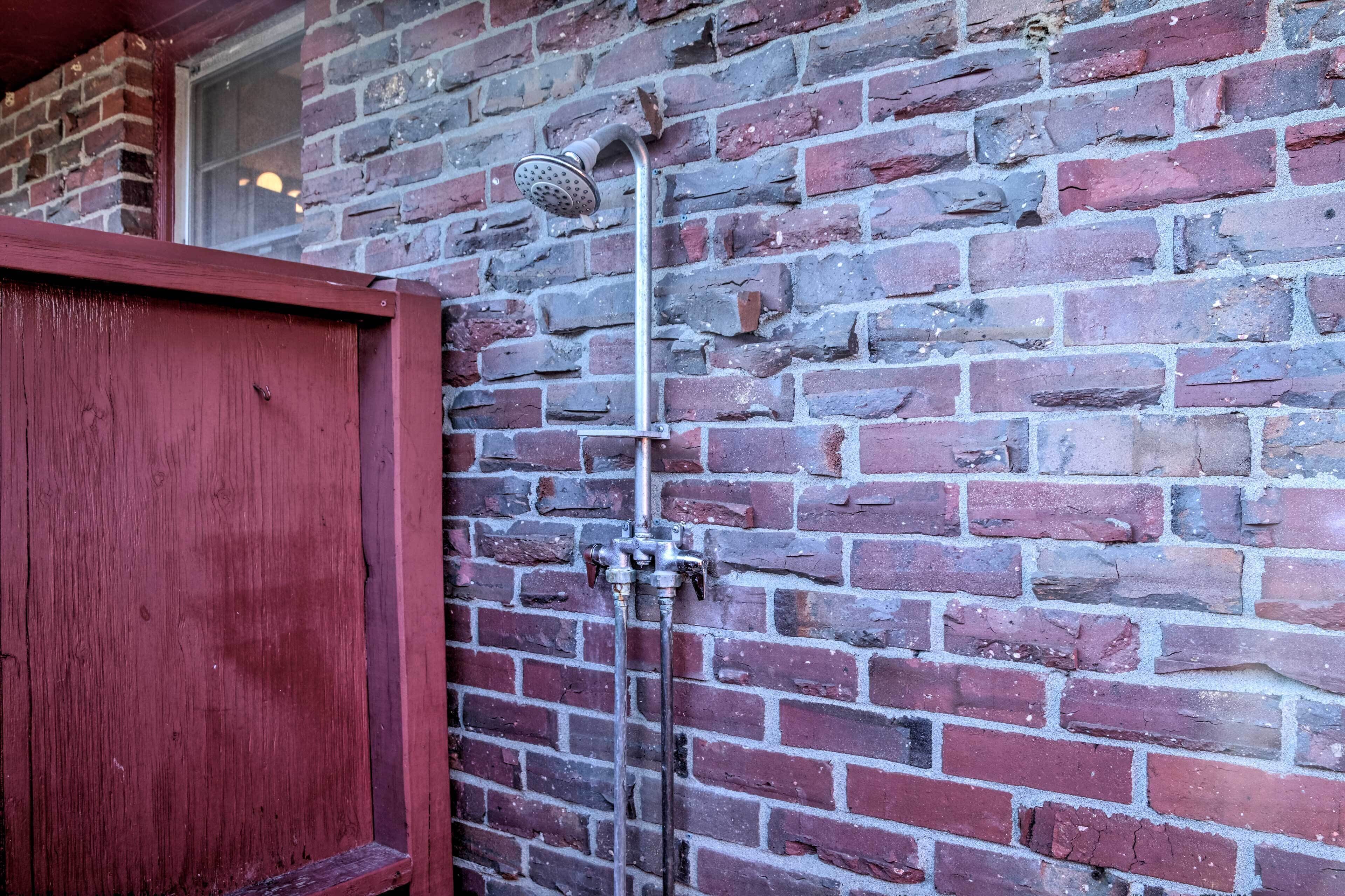 Una puerta de madera roja y un cabezal de ducha metálico adherido a una pared de ladrillo.