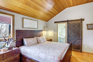 A bedroom with a wooden ceiling, a bed with a floral bedspread, a bedside table with a plant, and a sliding door. - Deck & Game Room: Family Wilmington Retreat (Wilmington)