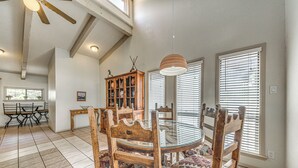 A dining area with a round glass table, wooden chairs with patterned cushions, a wooden cabinet, and a ceiling fan. - Ruidoso Home w/ Private Wet Bar & Pool Table (Ruidoso)
