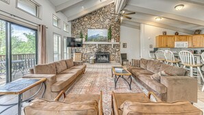 A spacious living area with a stone fireplace, comfortable seating, and a view of the outdoors. - Ruidoso Home w/ Private Wet Bar & Pool Table (Ruidoso)