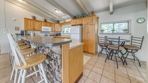 A kitchen with wooden cabinets, a granite countertop, and a dining area with metal chairs. - Ruidoso Home w/ Private Wet Bar & Pool Table (Ruidoso)