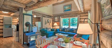 A cozy cabin interior with a dining area, a living room with blue sofas, a wood-burning stove, and a kitchen.