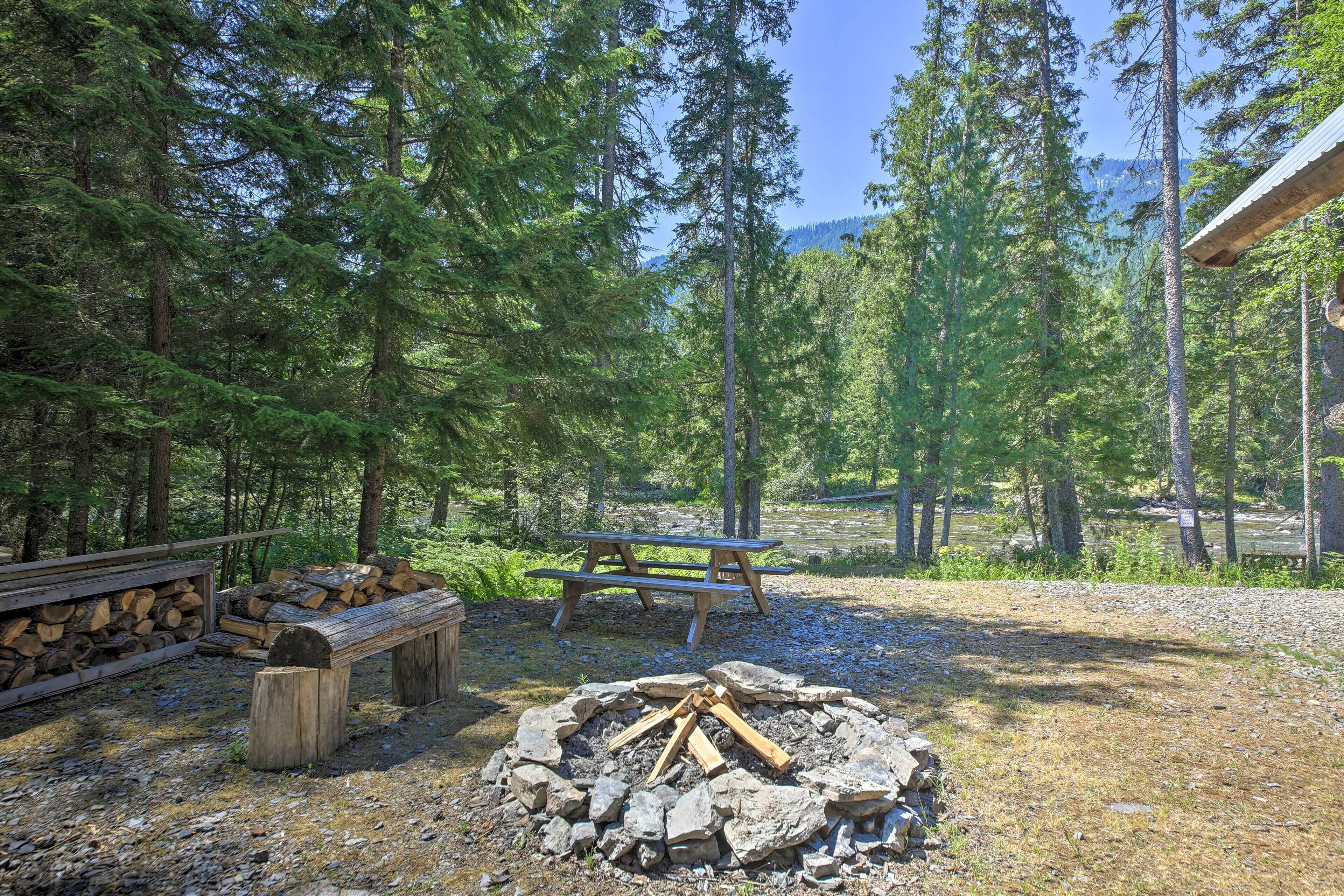 Een bosrijke kampeerplek met een vuurkuil, picknicktafel en een stapel hout.
