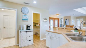 A kitchen with white cabinets, a wooden countertop, a clock, and a view into the dining area.