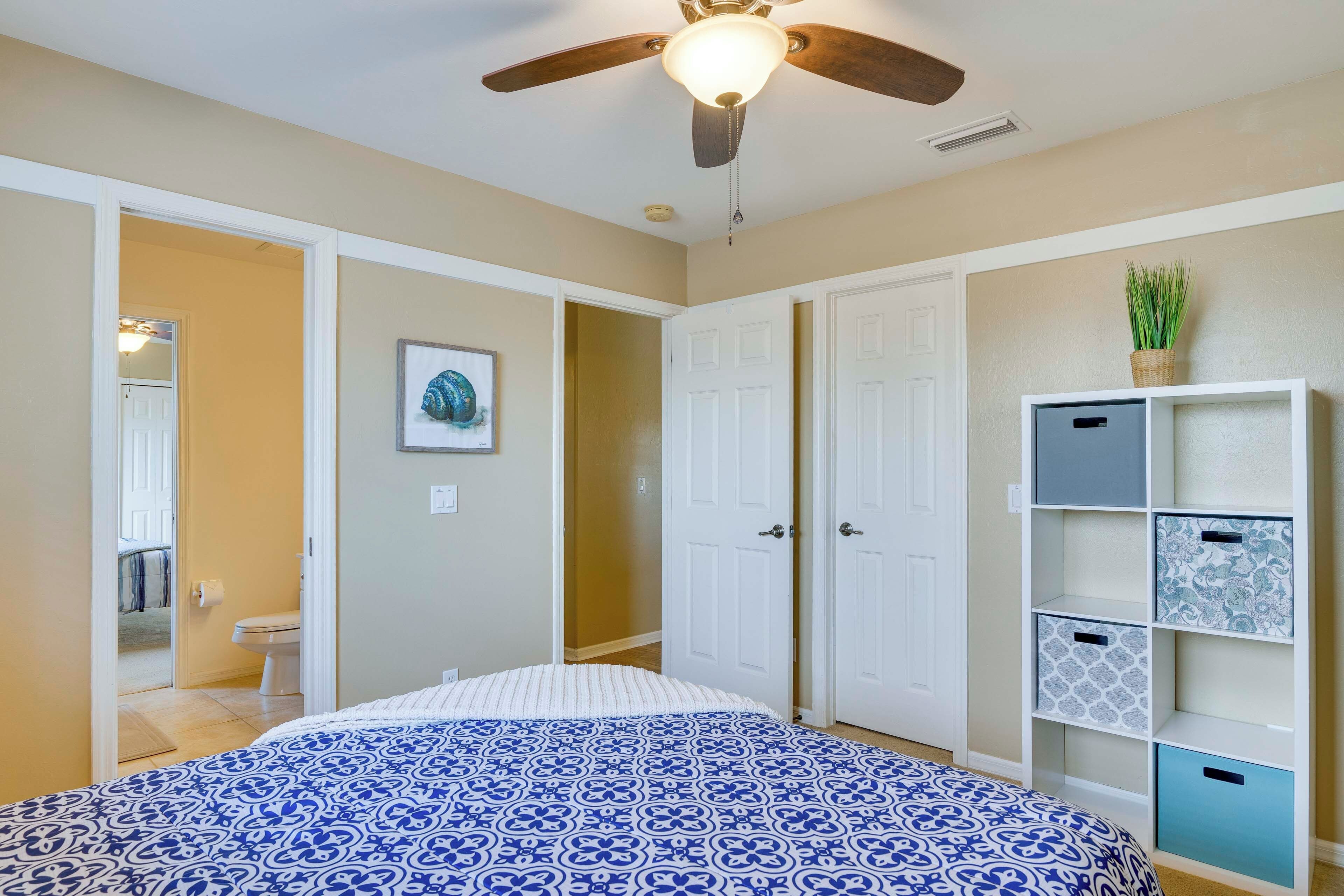 Un dormitorio con cama, ventilador de techo, armario blanco y estantería.