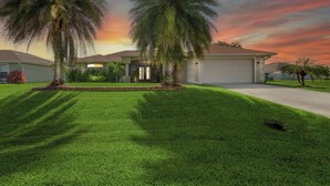A residential house with a well-maintained lawn, two palm trees, and a garage.