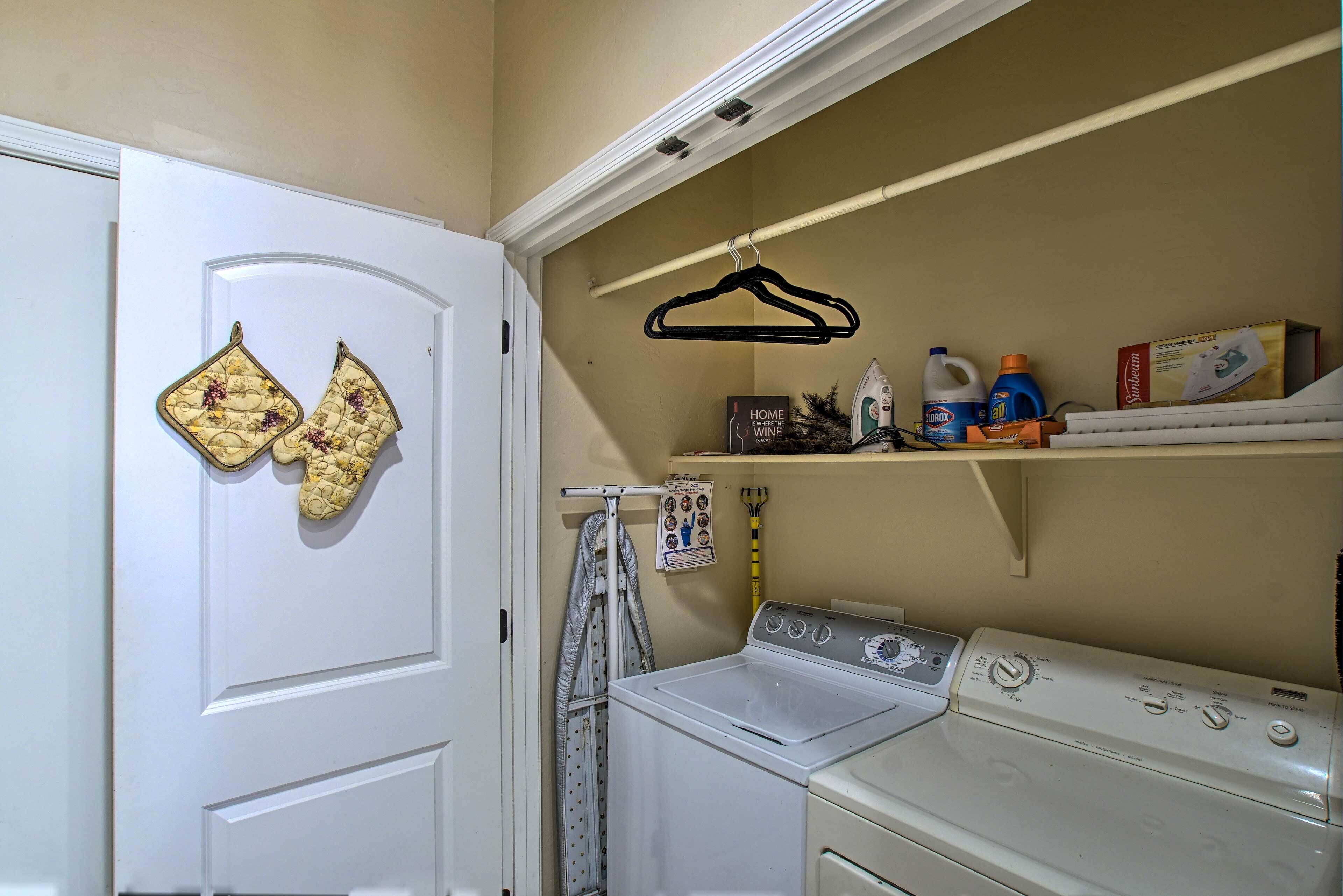 A laundry room with a washer and dryer, a drying rack, and shelves with cleaning supplies.