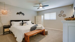 A bedroom with a bed, a wooden bench, a ceiling fan, a nightstand, a dresser, and decorative wall art. - Beautiful Phoenix Vacation Rental w/ Private Pool! (Phoenix)