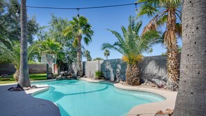 A swimming pool with a basketball hoop, surrounded by palm trees and a stone wall. - Beautiful Phoenix Vacation Rental w/ Private Pool! (Phoenix)