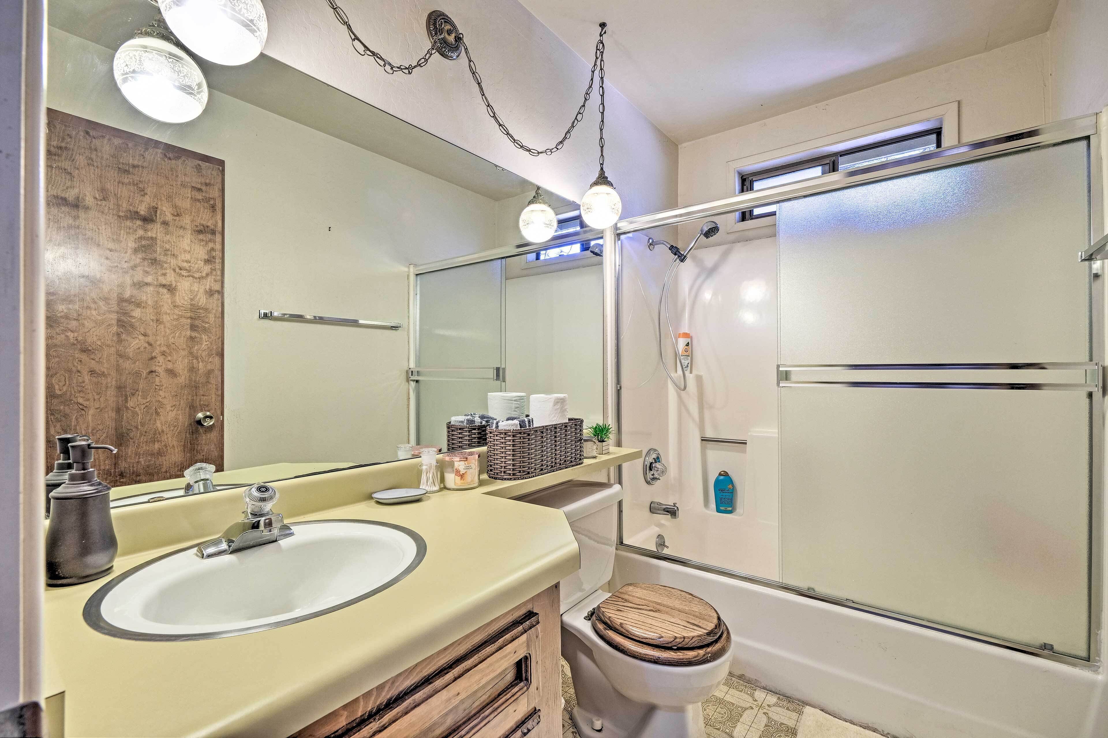 Une salle de bain équipée d’un lavabo, d’un miroir et de toilettes. Elle comprend également un espace douche avec une porte en verre et un pommeau de douche.