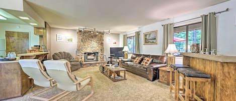 A cozy living room with a stone wall, a fireplace, a leather sofa, a wooden coffee table, and a bar area.