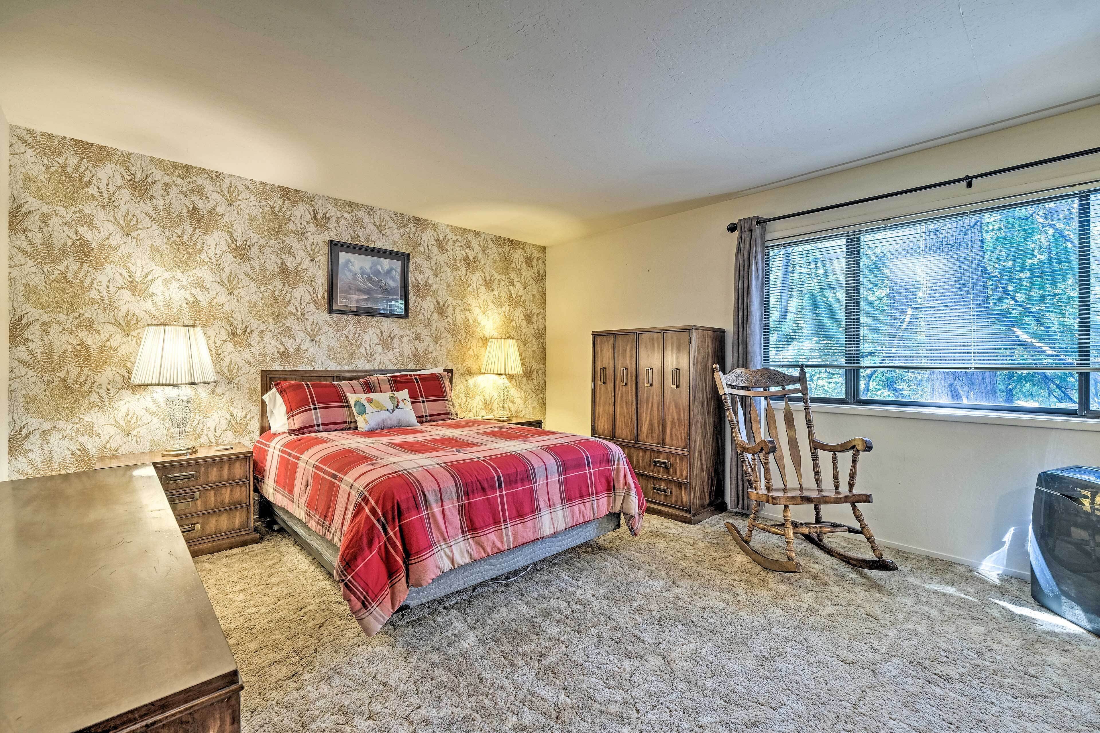 A bedroom with a bed, nightstands, a rocking chair, a wooden wardrobe, and a window with blinds.