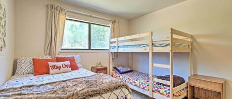 A bedroom with a large bed, a smaller bunk bed, a nightstand, and a window with curtains.