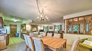 Ein geräumiger Essbereich mit einem Holztisch und Stühlen, einer Chandelüster und Blick auf Küche und Wohnzimmer.