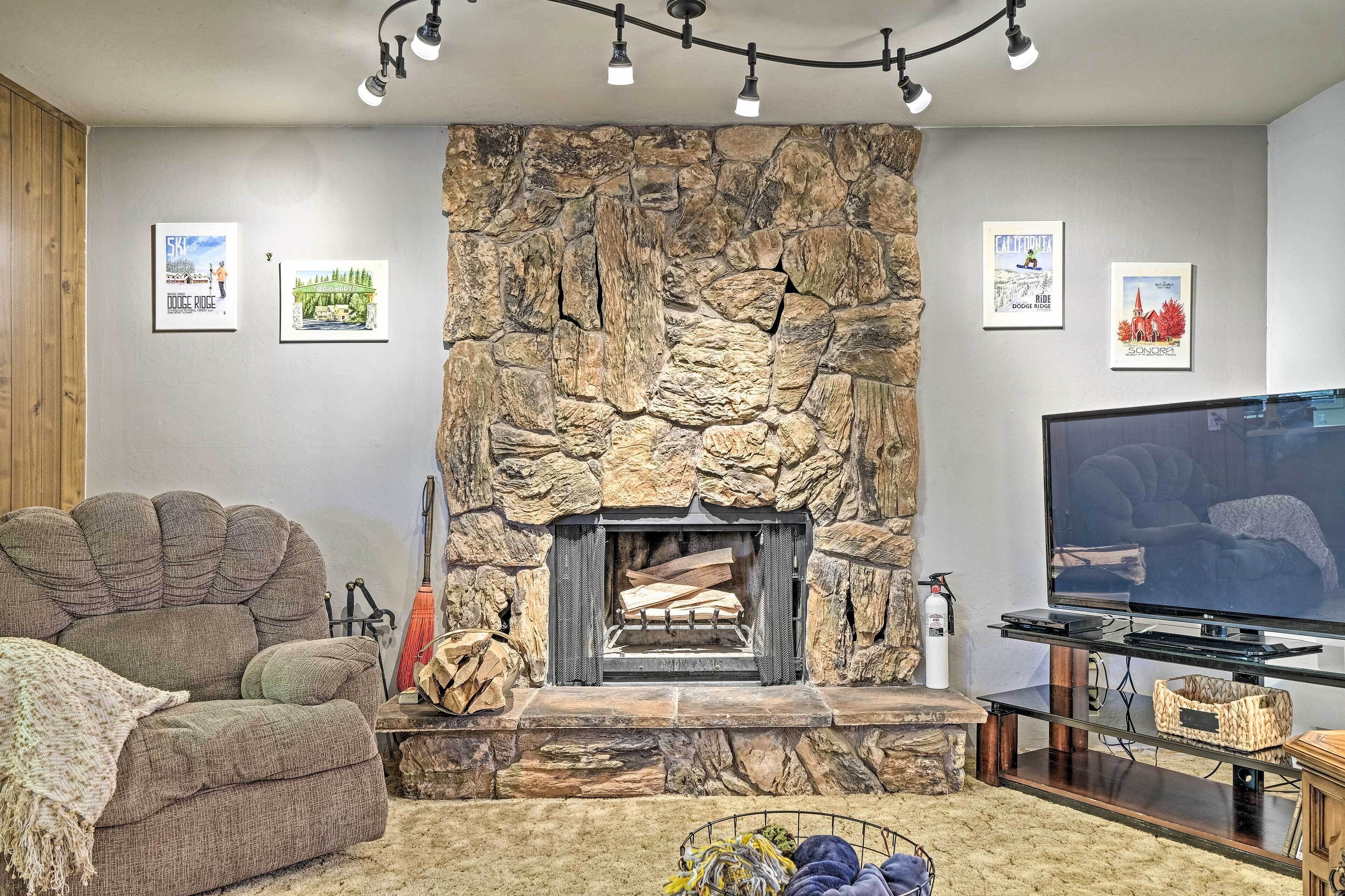 A living room with a stone fireplace, a large flat-screen TV, and a cozy couch.