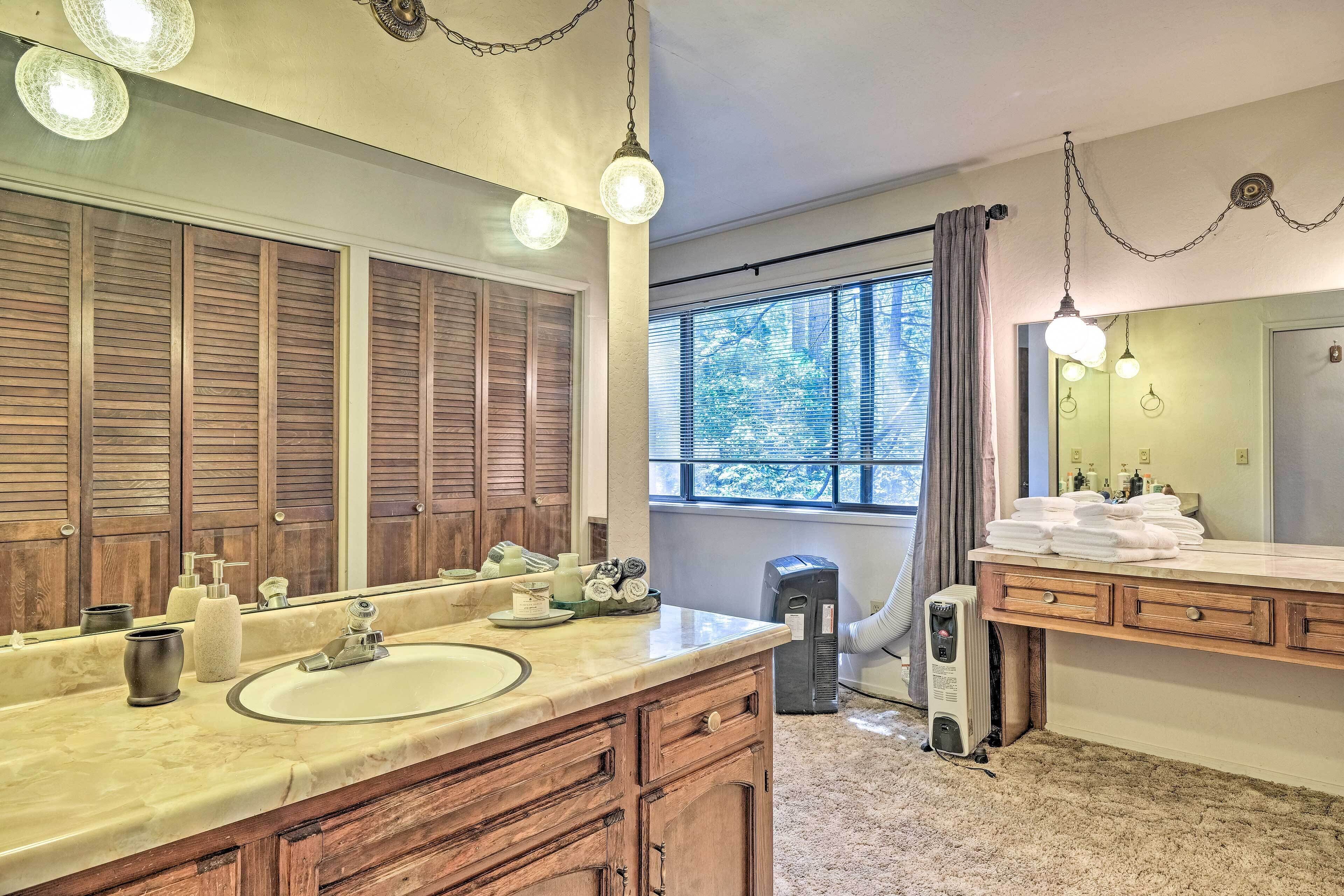 A bathroom with two sinks, wooden cabinets, a large mirror, and a window with a view of trees.