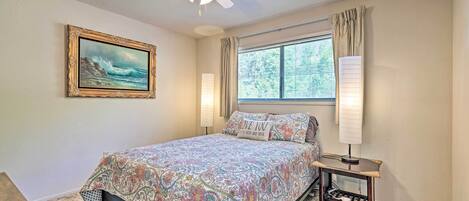 A bedroom with a bed, a ceiling fan, a window with curtains, a bedside lamp, and a framed picture on the wall.