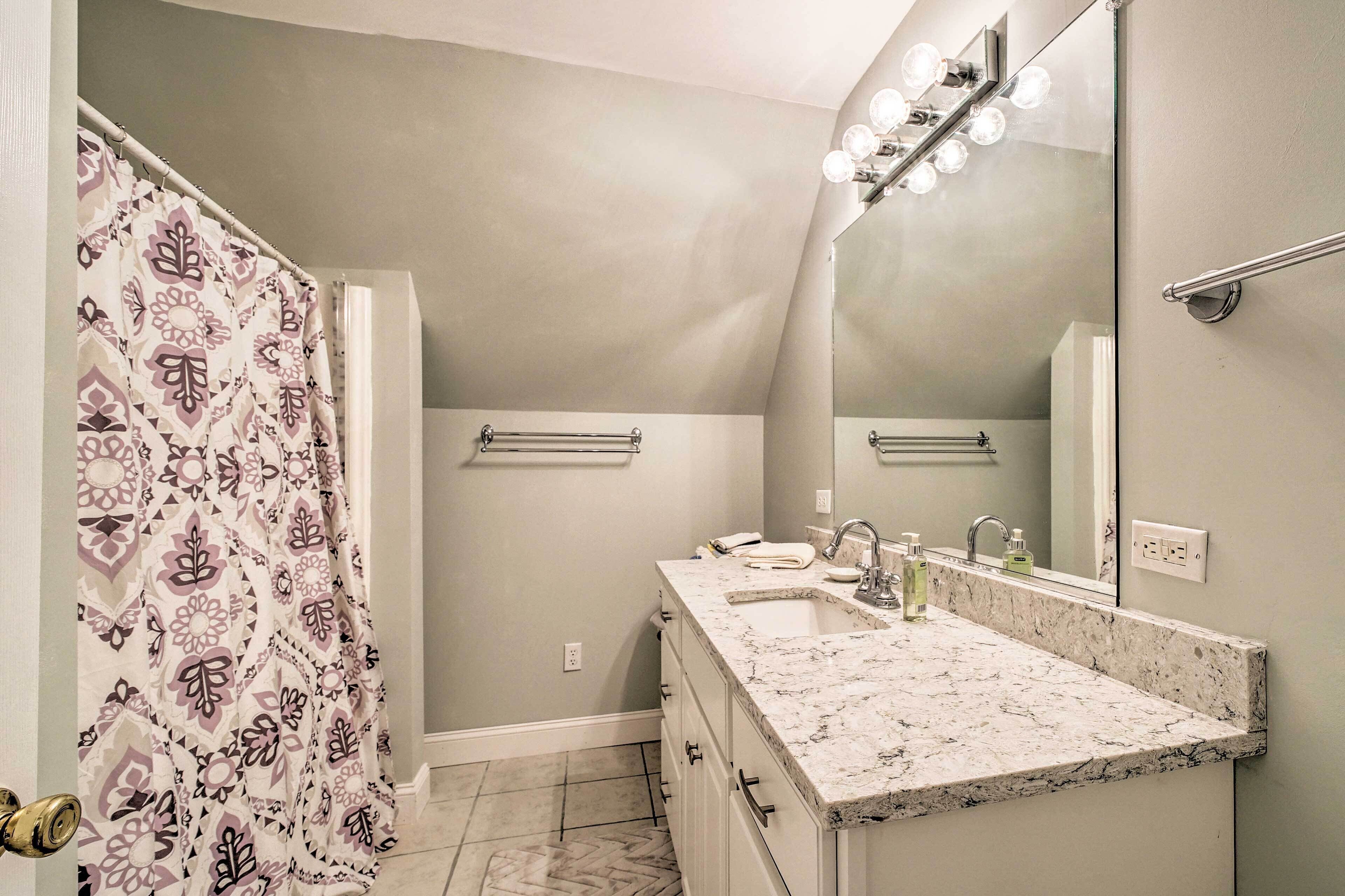 A bathroom with a shower curtain, a sink with a mirror, and a vanity with drawers.