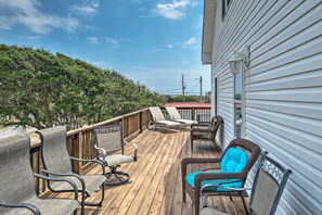 Um deck de madeira com móveis de exterior, incluindo cadeiras e uma mesa, com vista para uma área arborizada.