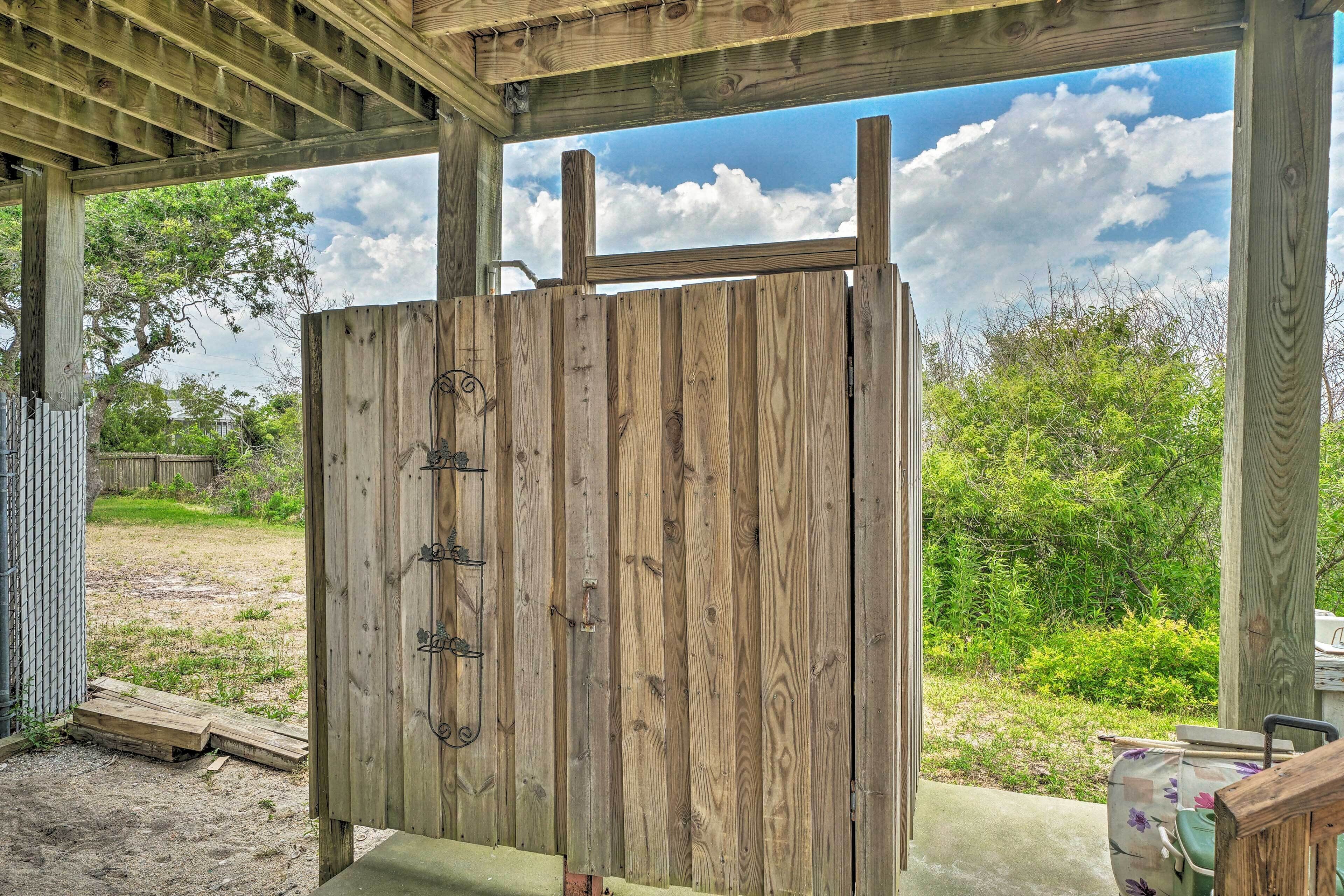 A wooden structure with a metal gate, a concrete floor, and a view of a grassy area with trees and a cloudy sky.